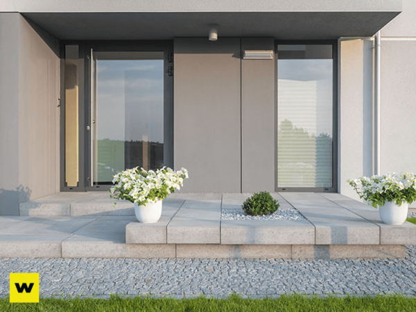 Moderner Hauseingang mit grauen Fliesen, Glasfront und weißen Blumenkübeln im Garten.